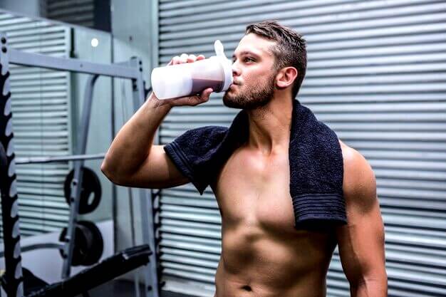 Jeune homme qui prend de la protéine à la salle de musculation